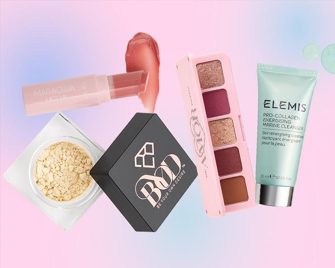 A flat lay of beauty products on a pink-to-blue gradient background, including Tarte Maracuja Juicy Lip, loose setting powder, BYOD compact, a LUNA MAGIC eyeshadow palette, and an ELEMIS cleanser.