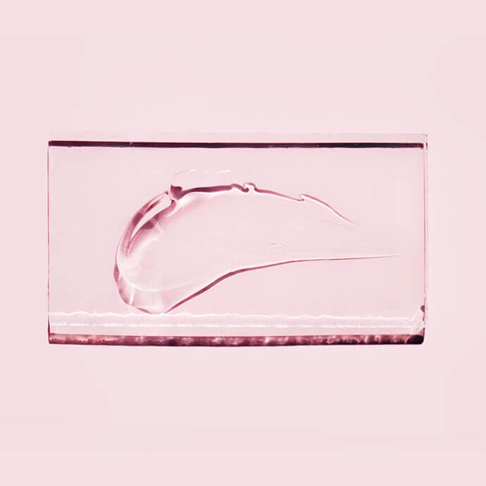 Smear of transparent gel on glass on pastel pink background