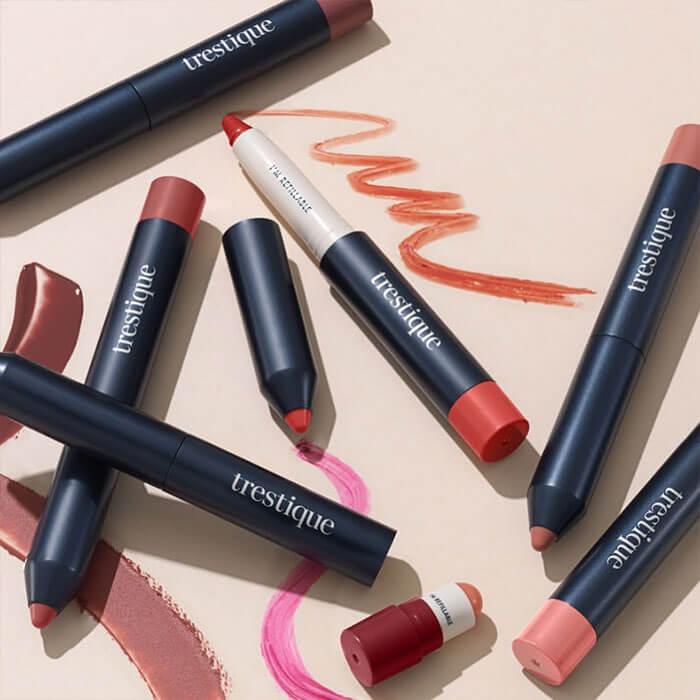 A flat lay featuring various lip crayons in an array of colors, with swatches displayed on a peach-colored background