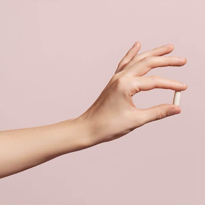 A close-up photo of a hand grasping a white tablet against a soft pink backdrop