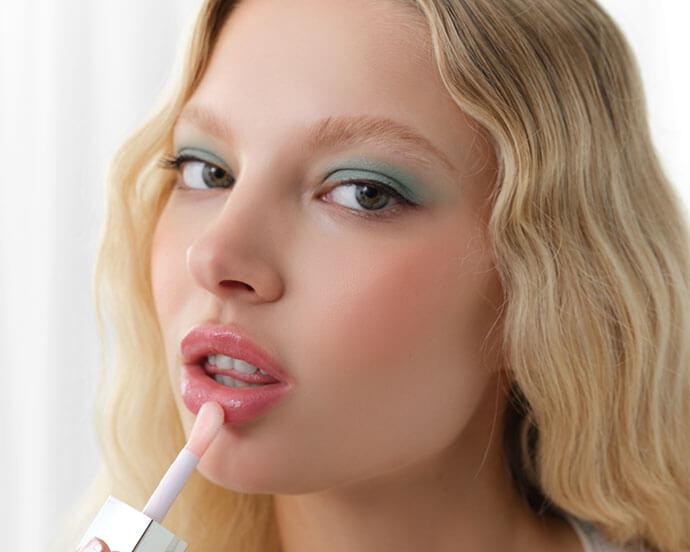 A close-up shot of a girl with light makeup gently applying lip plumper to her lips