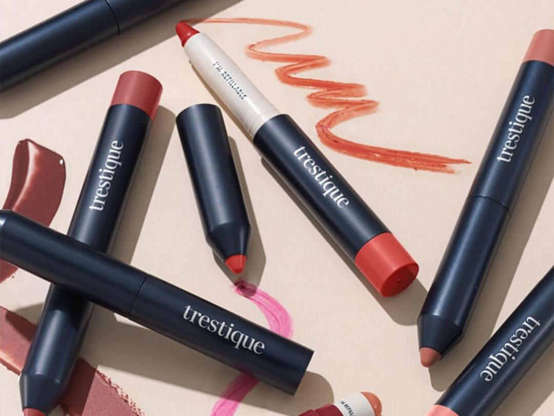 A flat lay featuring various lip crayons in an array of colors, with swatches displayed on a peach-colored background