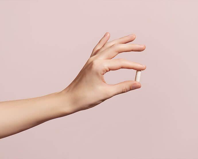 A close-up photo of a hand grasping a white tablet against a soft pink backdrop
