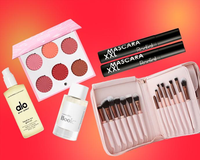 A flat lay of beauty products on a red-to-orange gradient background, featuring Alo Glow System body oil, Commodity Book perfume, Rodial XXL mascara, a blush palette, and a pink brush set in a zip-up case.