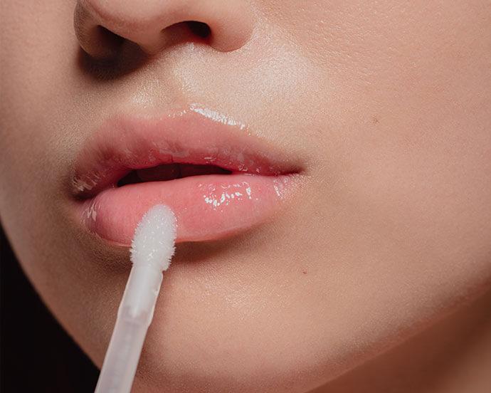 A close-up image of glossy, pouty lips with a lip gloss applicator in view