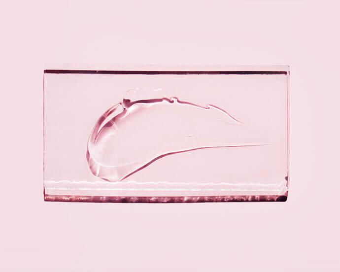 Smear of transparent gel on glass on pastel pink background