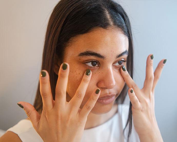 An image of a woman gently touching her under-eye area with her black-painted nails