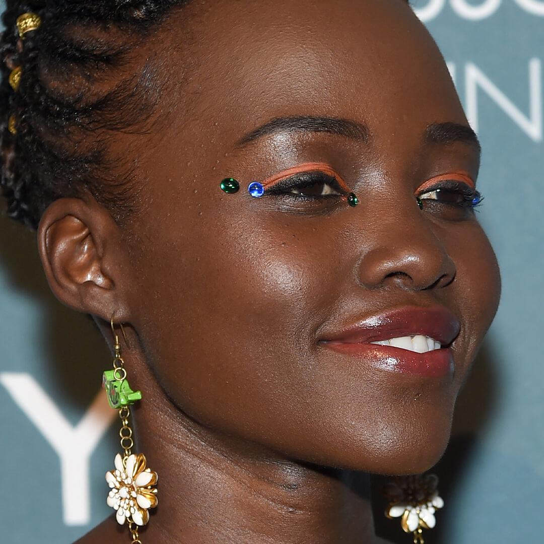 Lupita Nyong'o rocking an orange eyeliner look studded with blue and green gemstones Mobile
