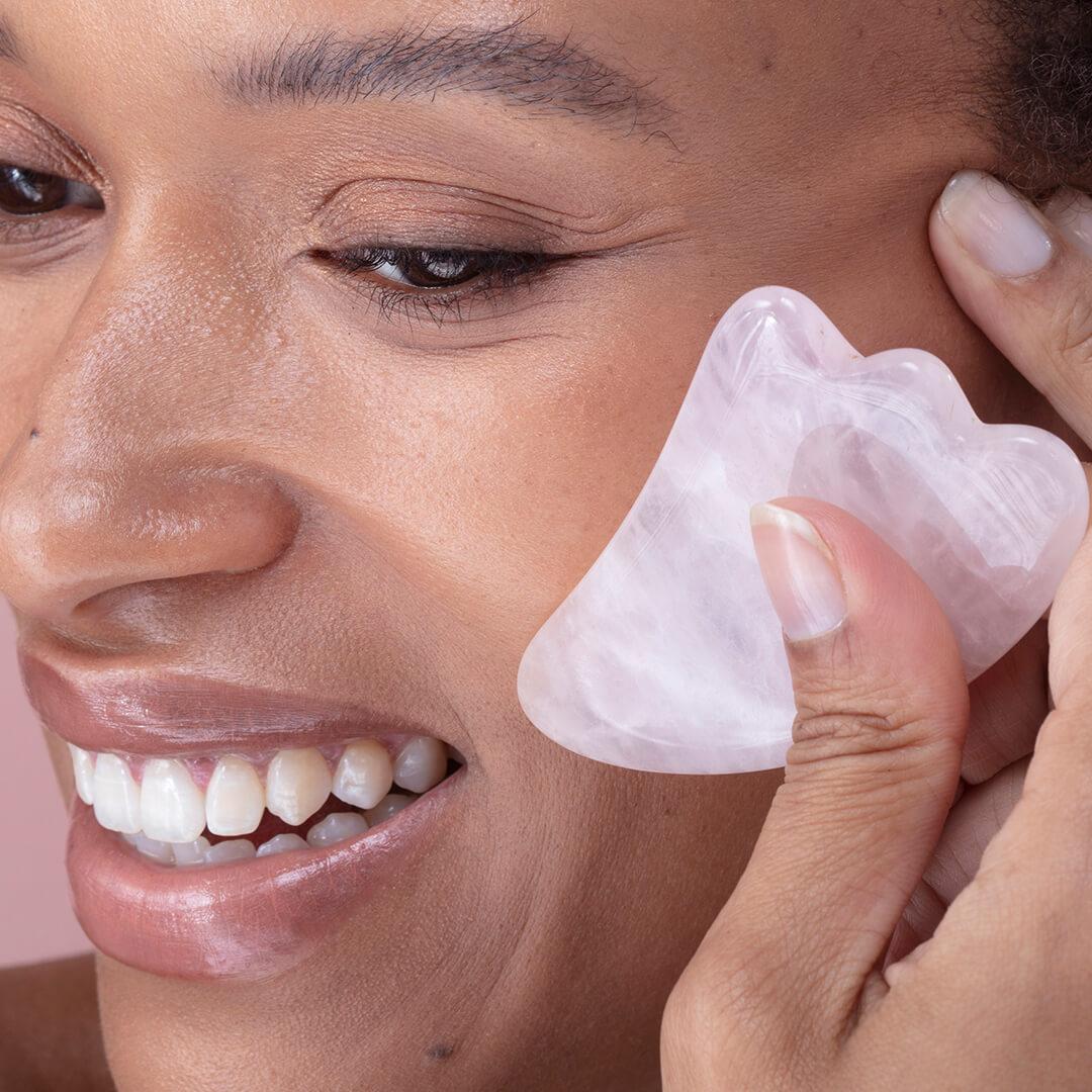 Close-up image of a woman using a pink quartz gua sha stone on her face Mobile