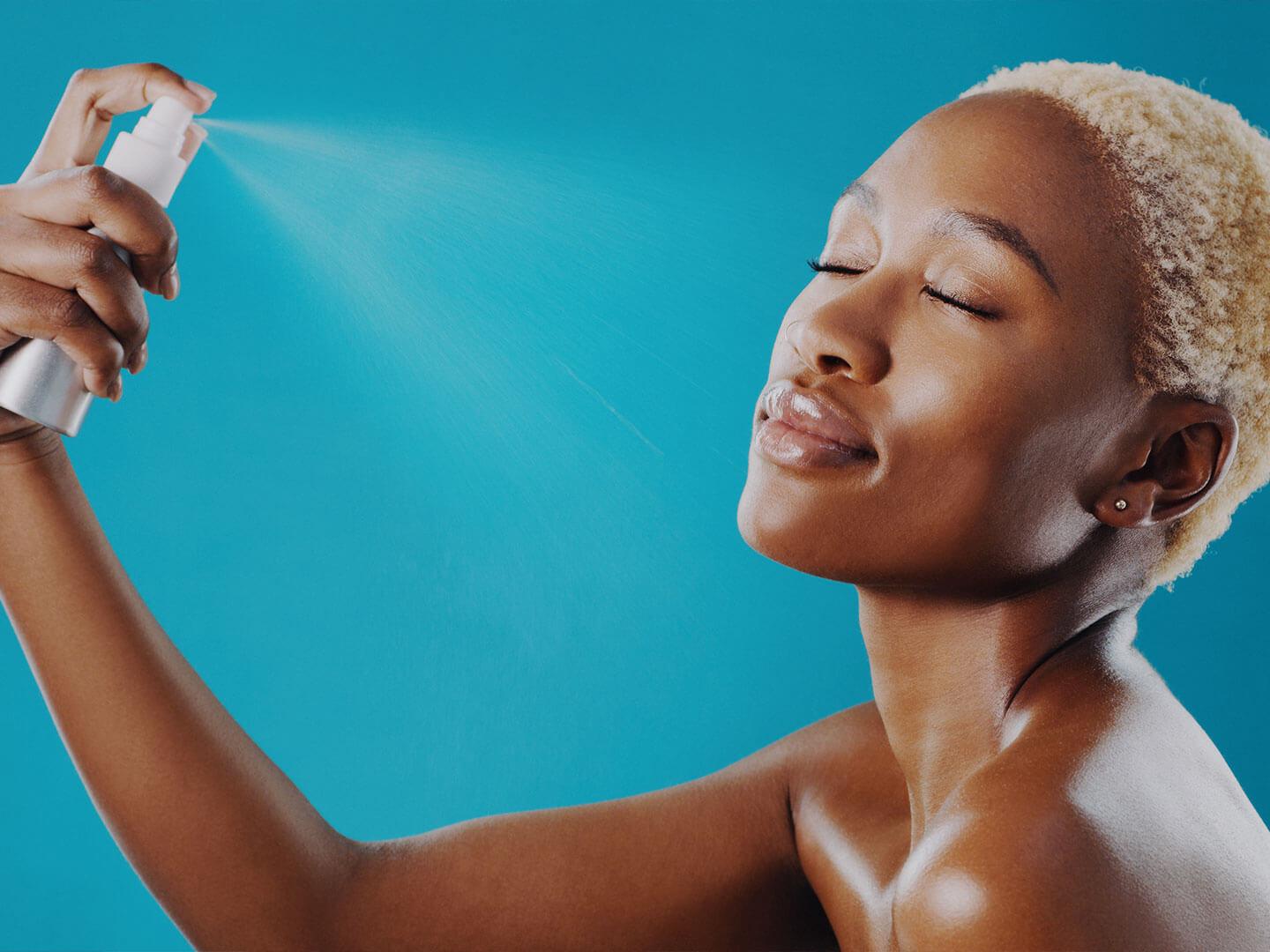 An image of a young woman of color, misting a setting spray onto her face Desktop