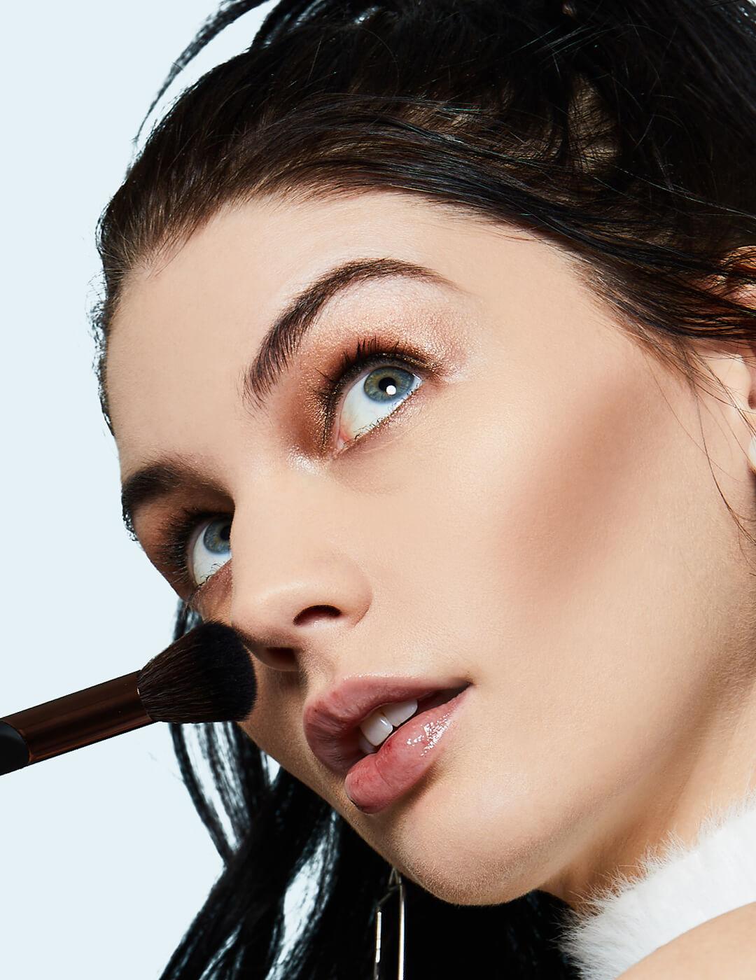 Close-up of model applying setting powder on her nose using a black powder brush Desktop