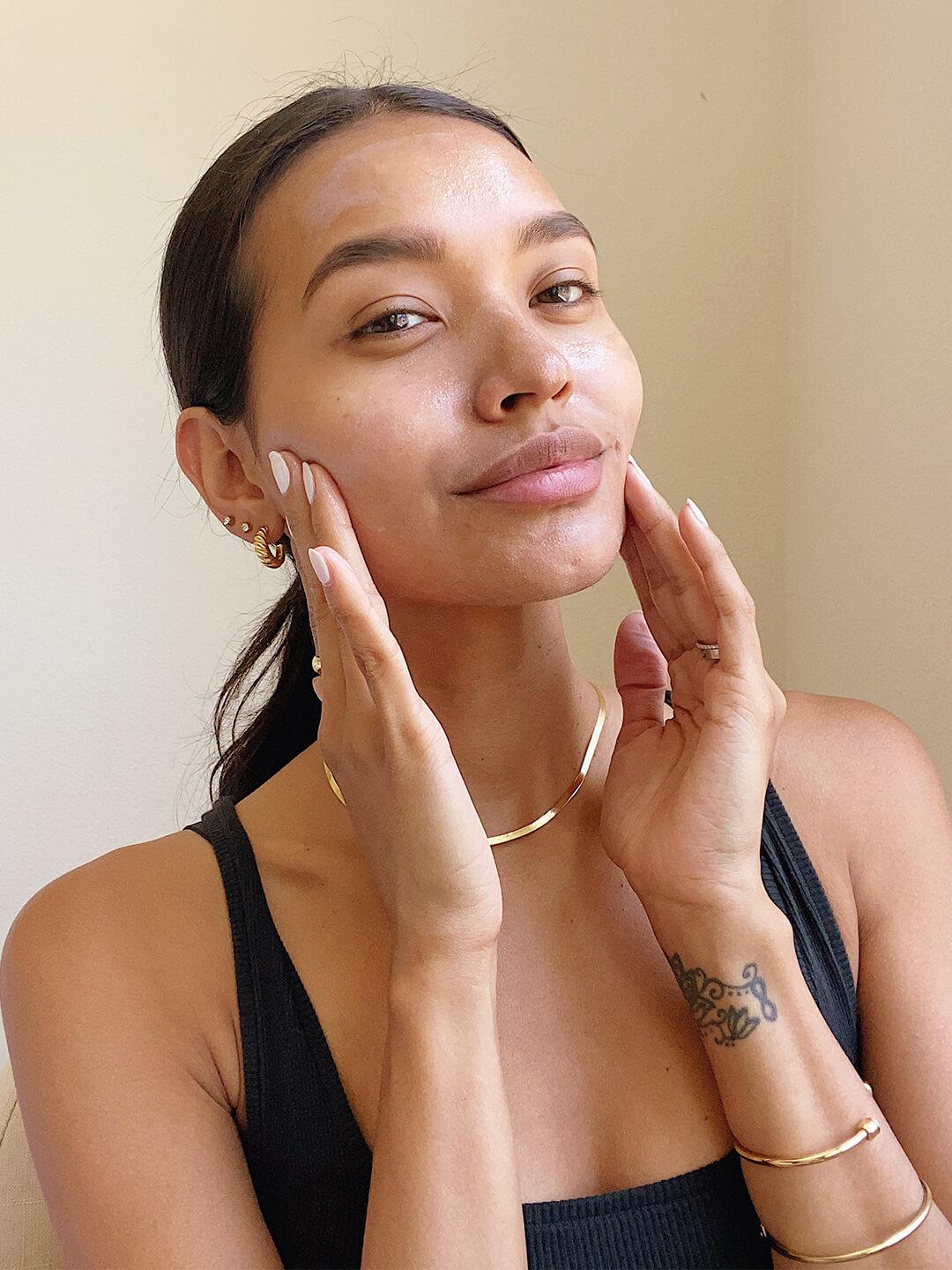 Close-up image of a model in black tank top touching her cheeks while smiling