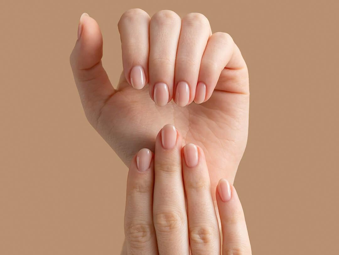 Hands of a beautiful well-groomed woman with feminine nails on a beige background. Desktop
