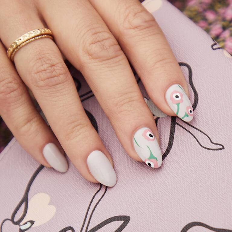 Close-up of a model's hand with hand drawn poppies nail art holding the April 2020 IPSY Glam Bag Desktop