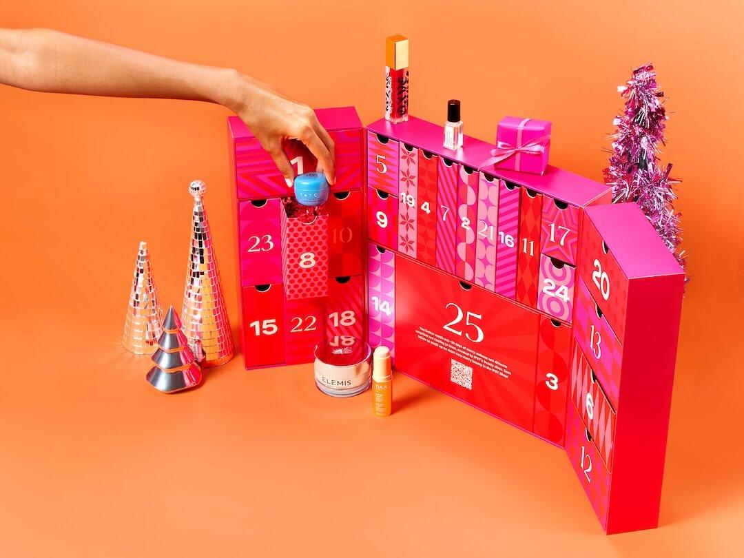 IPSY 2024 Beauty Advent Calendar open on an orange background with a hand reaching in Desktop