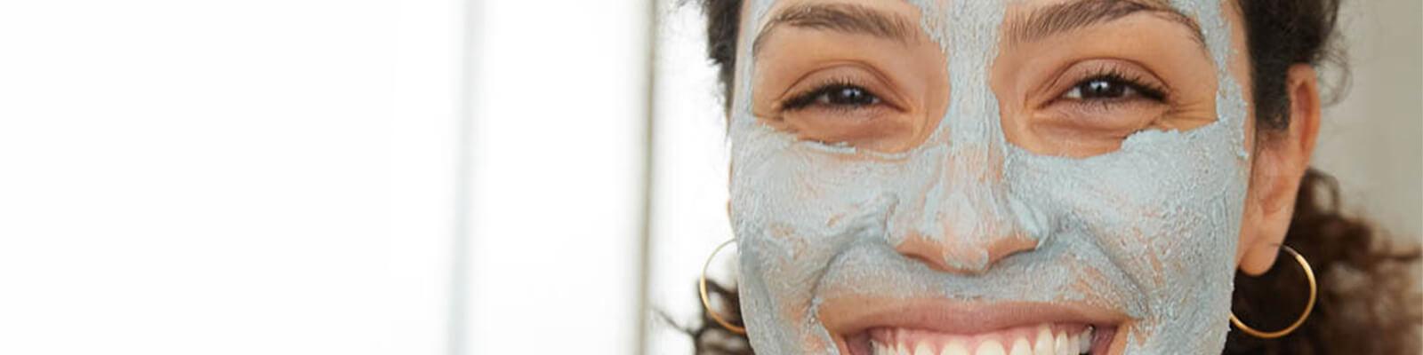 An image of a model with mud mask on her face smiling big