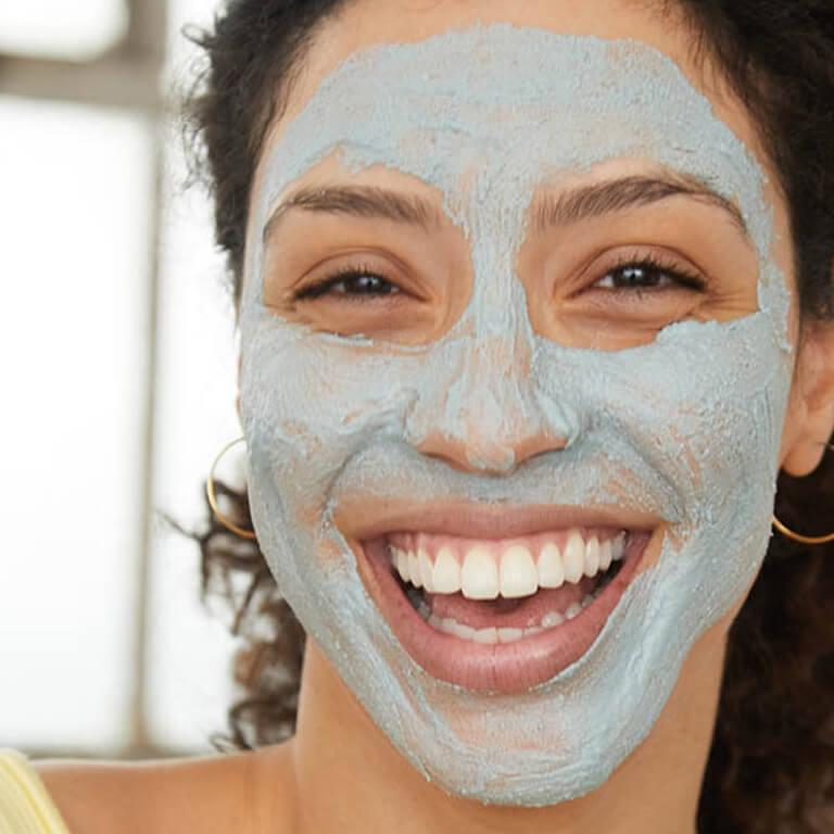 An image of a model with mud mask on her face smiling big