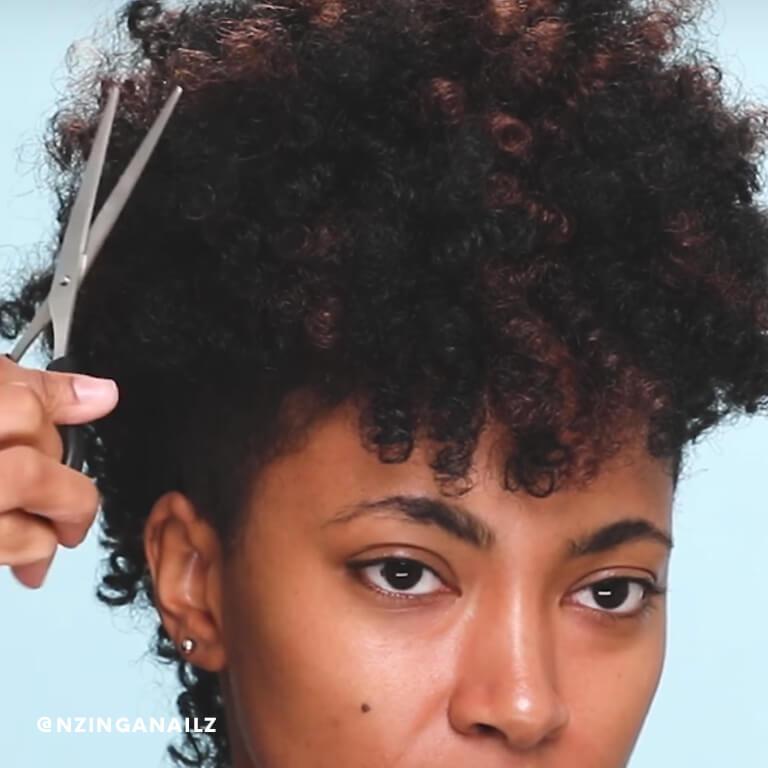 A hairstylist trims excess hair from Nzinga Nailz' crochet braids.  Desktop