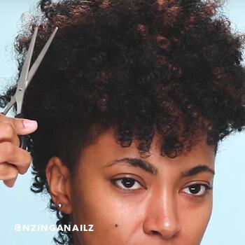 A hairstylist trims excess hair from Nzinga Nailz' crochet braids.  Mobile
