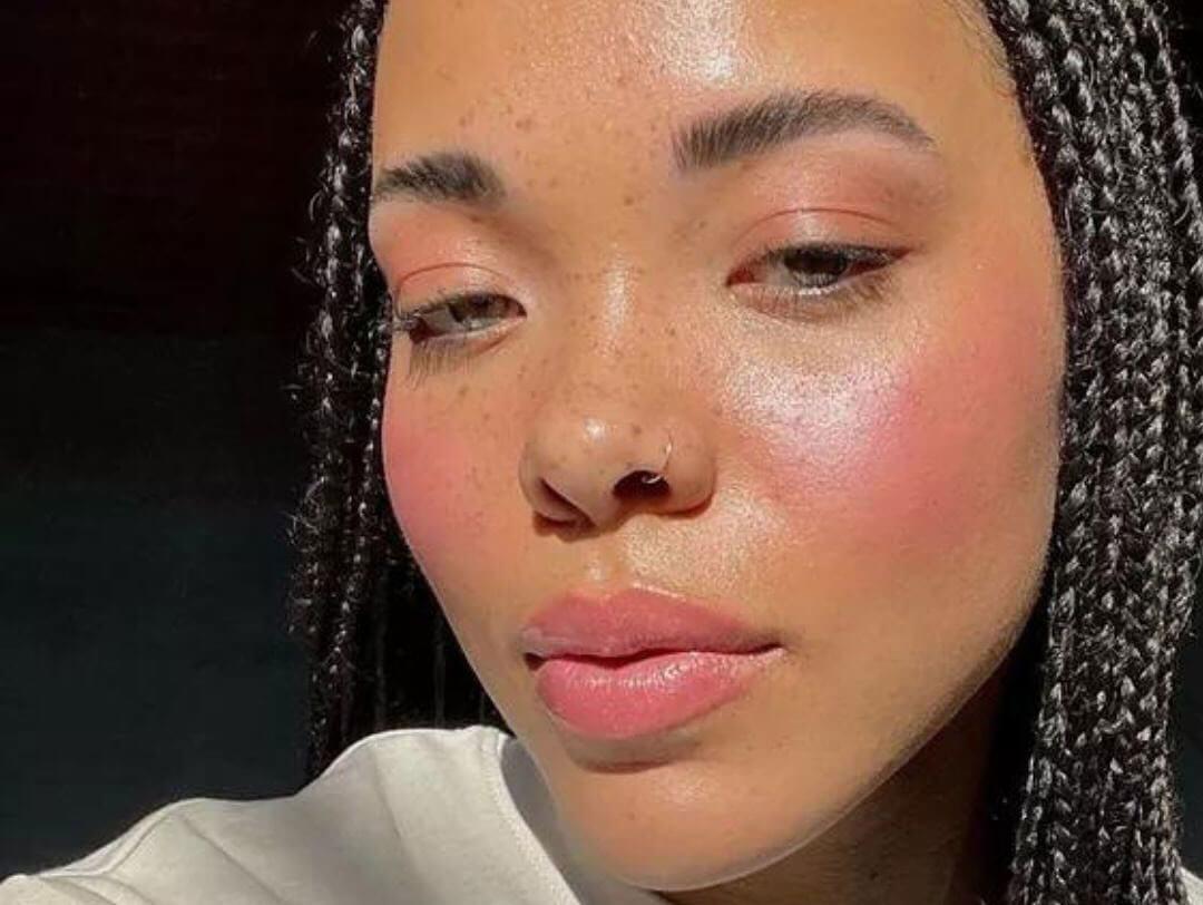 A close-up image of a woman with her box braids down, showcasing her nose ring, while wearing a boyfriend blush