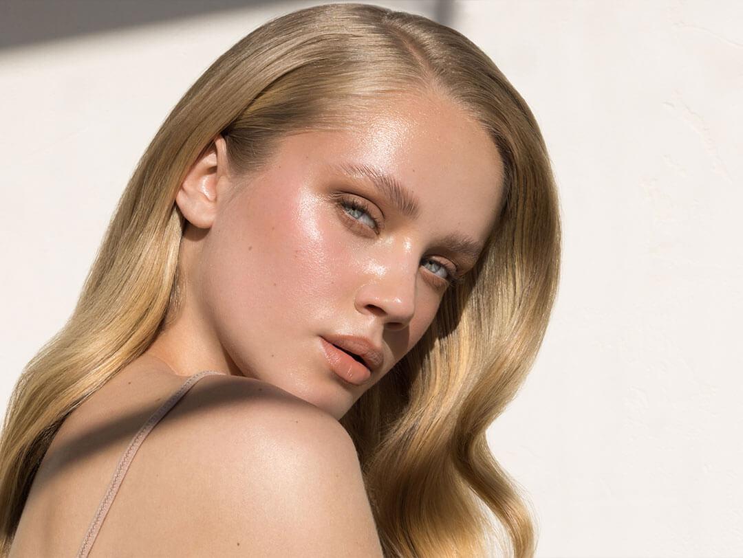 Blonde woman with flawless, radiant skin and glossy makeup, exemplifying the "pearl skin" effect with a luminous, dewy finish
