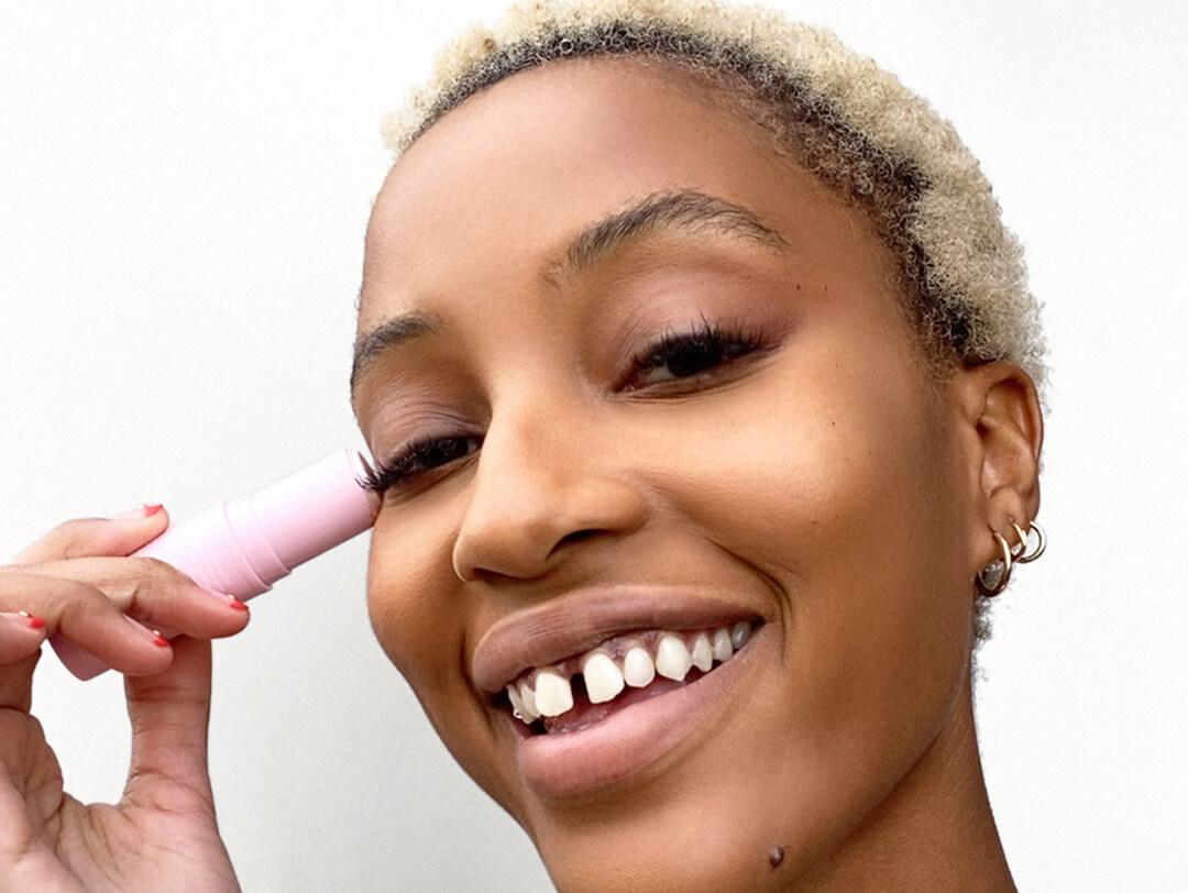 Close-up of a Black female model holding a cream highlighter against her temple
