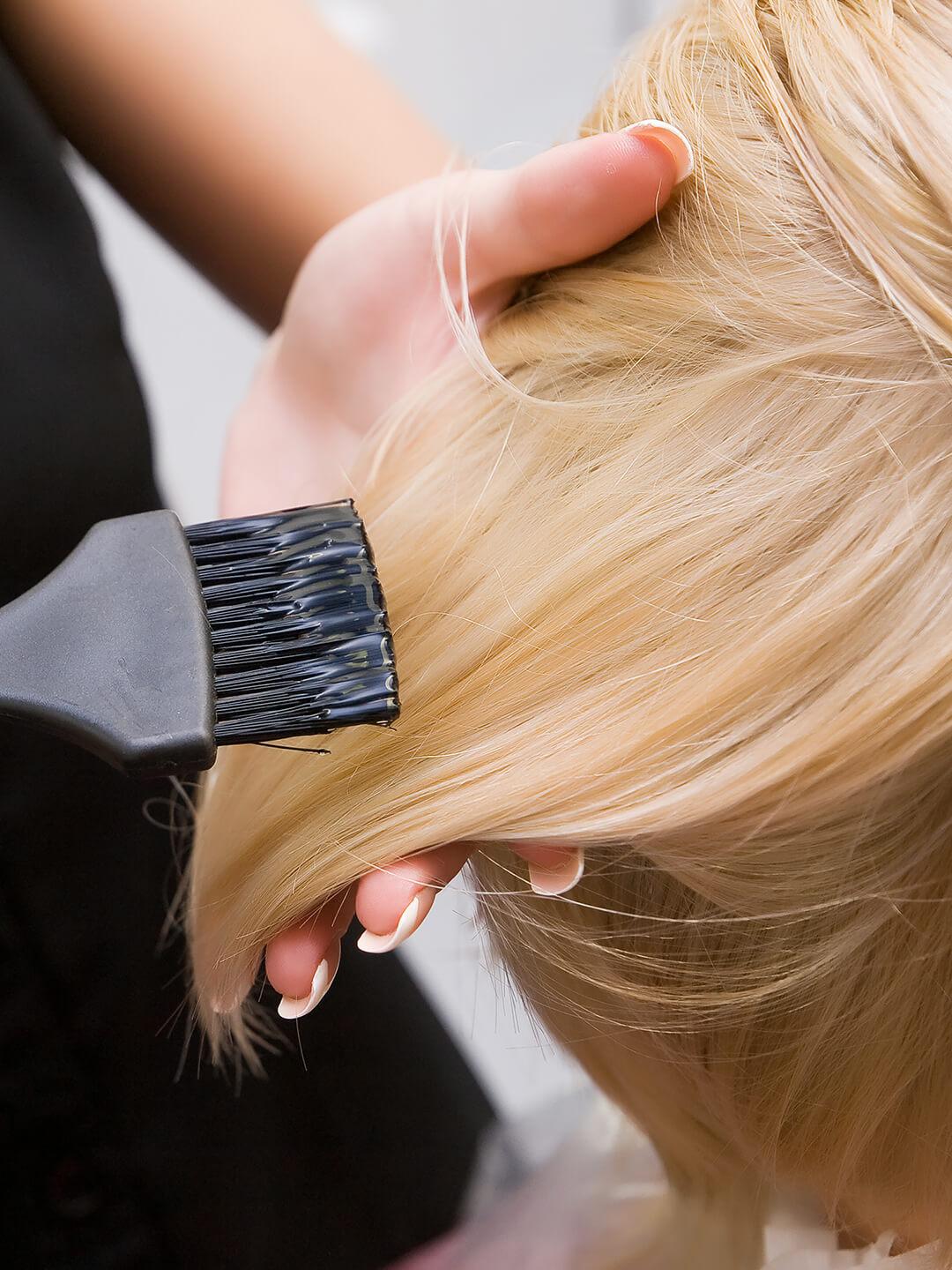 Close-up of a hair colorist applying product on a woman's blonde hair using a brush Desktop