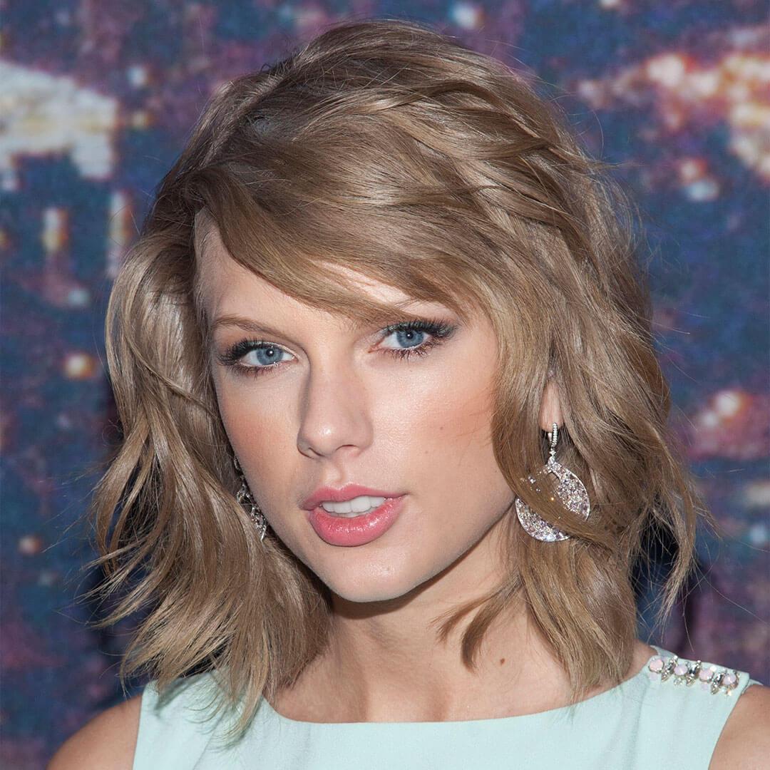 An image of Taylor Swift with her short, wavy hair and minimal makeup that includes teal eyeshadow and peachy lipstick, clad in a teal top Mobile