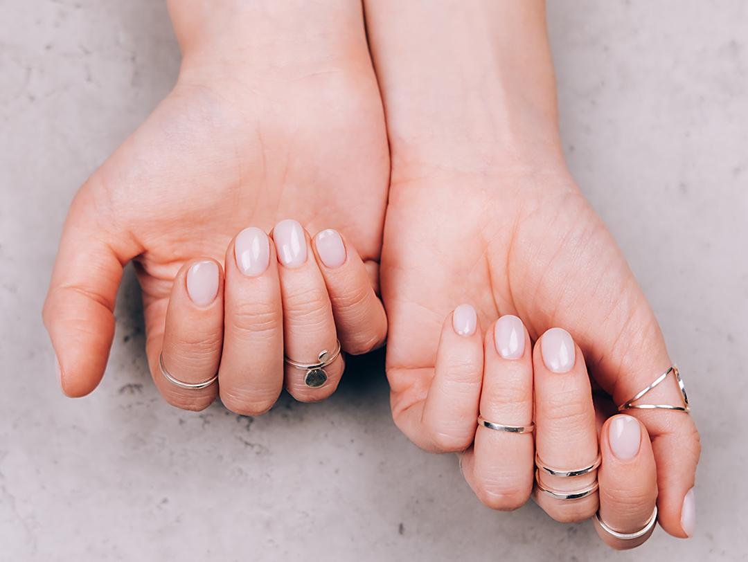 Close-up image of woman's hands wearing different gold rings with cream-colored nail manicure