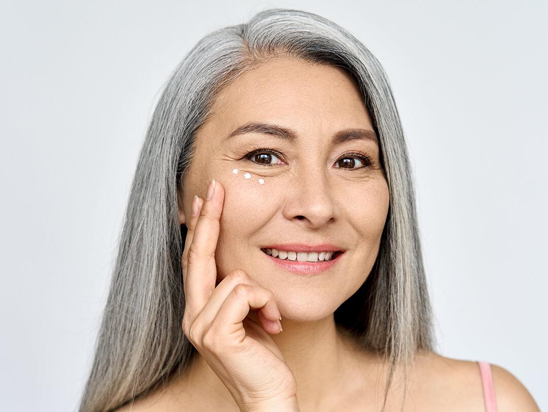 An image of a middle-aged woman looking fresh in her white hair while touching her cheeks on a gray background Desktop