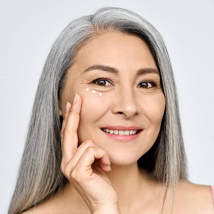 An image of a middle-aged woman looking fresh in her white hair while touching her cheeks on a gray background Mobile