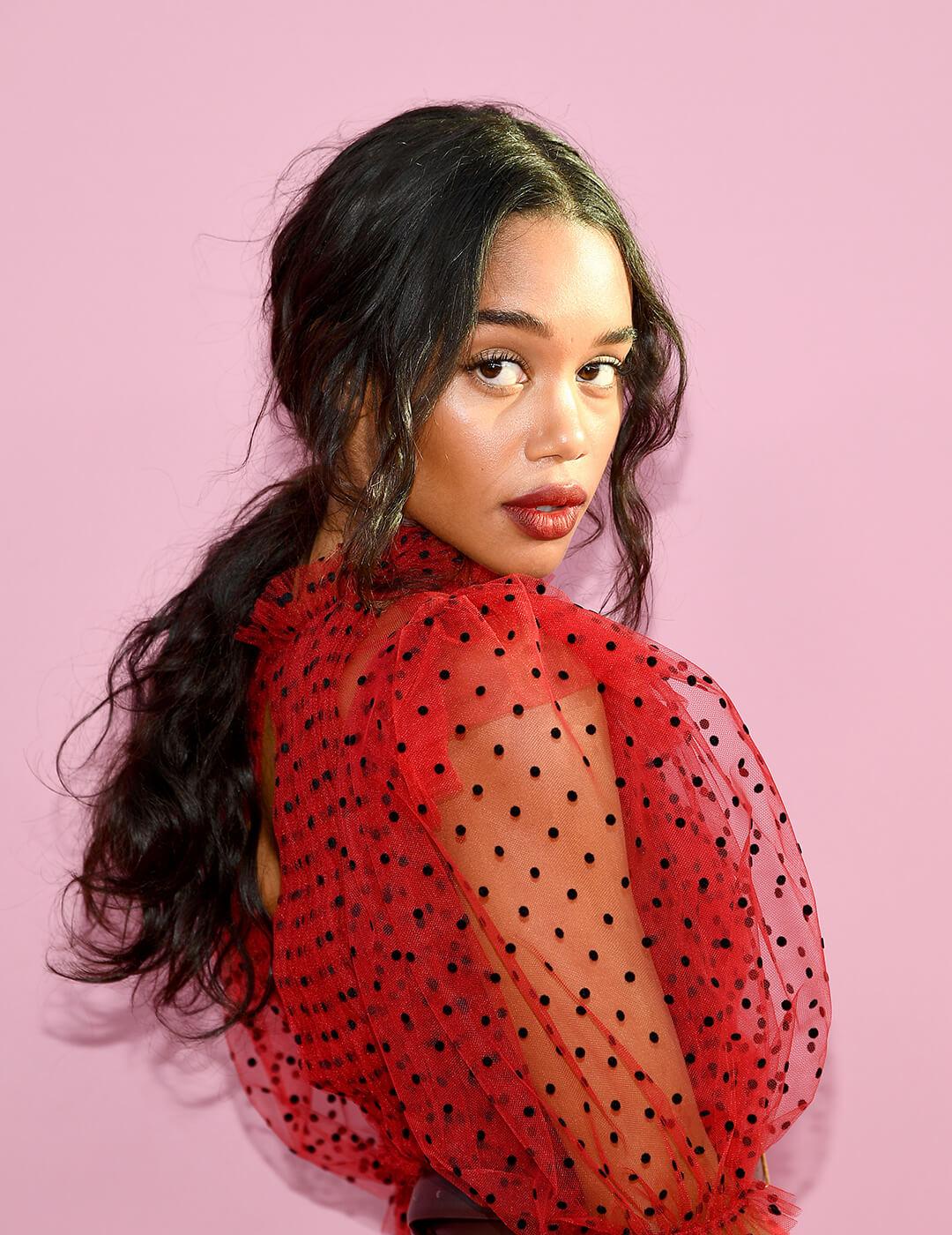 A photo of Laura Harrier sporting her black long hair in a modern romance ponytail wearing a red dress with a puffed see through sleeve in polkadots Mobile