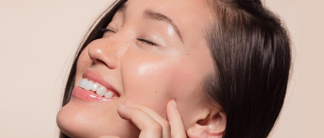 Young woman touching her face while smiling with closed eyes
