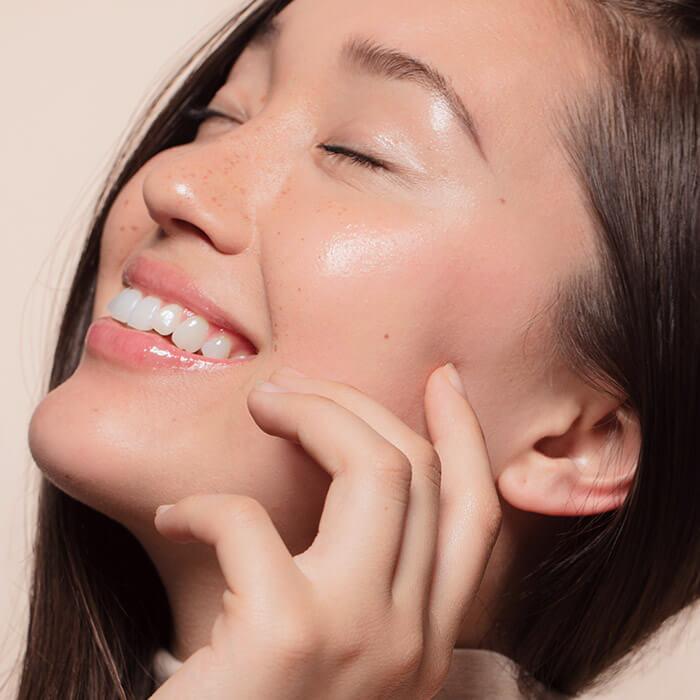 Young woman touching her face while smiling with closed eyes