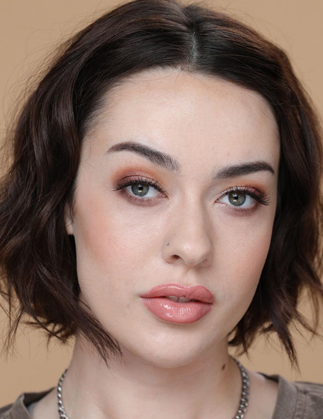 A photo of a woman with curly brunette hair wearing a light makeup on a hazel-colored background Mobile