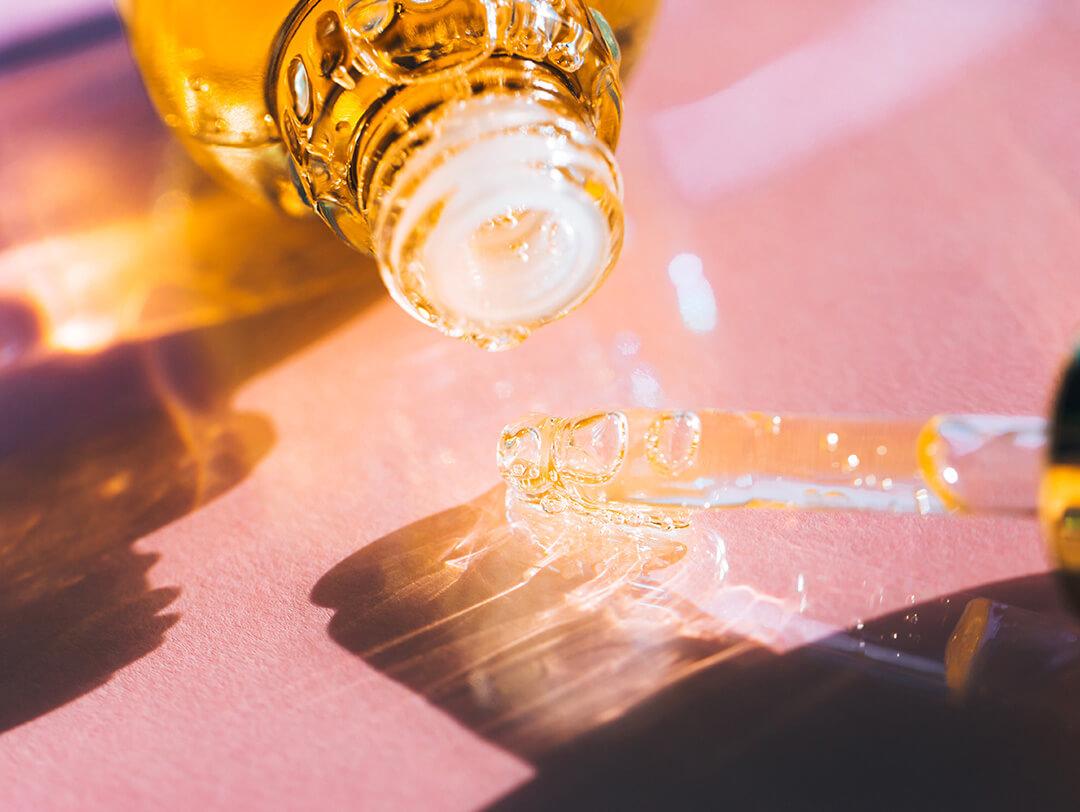 Glass bottle and pipette with bright yellow essential oil placed on pastel pink background Desktop