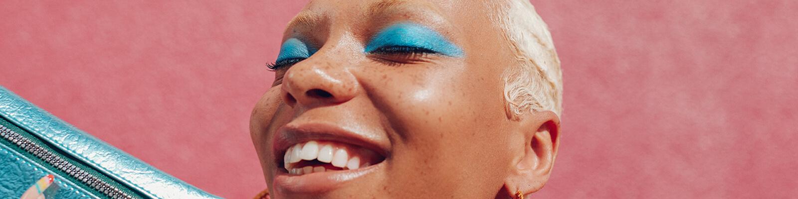 An image of a model wearing turquoise blue eyeshadow while holding a metallic turquoise blue Glam Bag