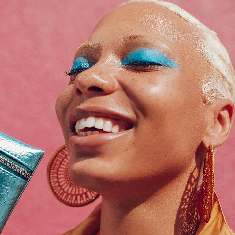 An image of a model wearing turquoise blue eyeshadow while holding a metallic turquoise blue Glam Bag