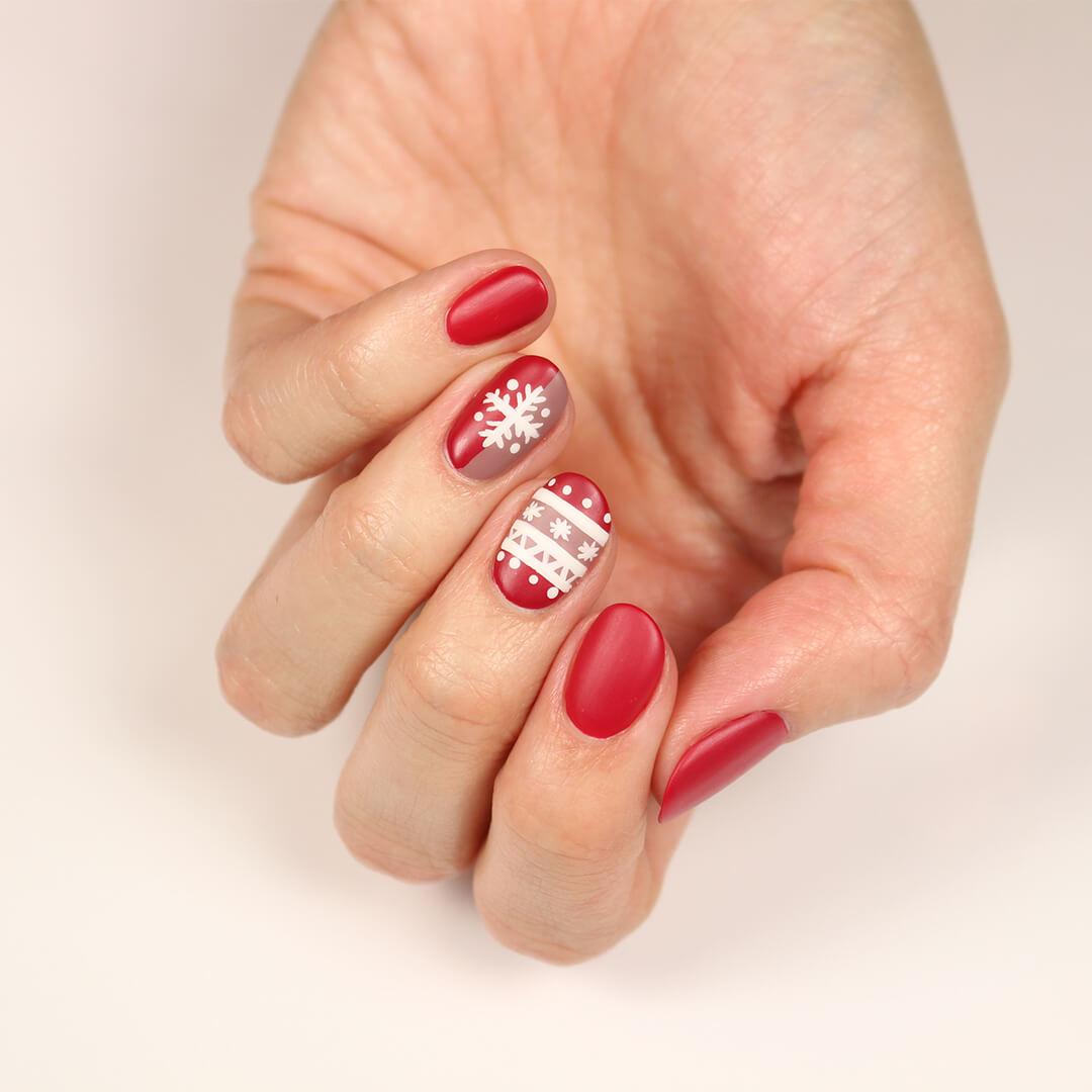 Image of a model's hand with a red and white snowflakes and sweater themed nail art mani Desktop