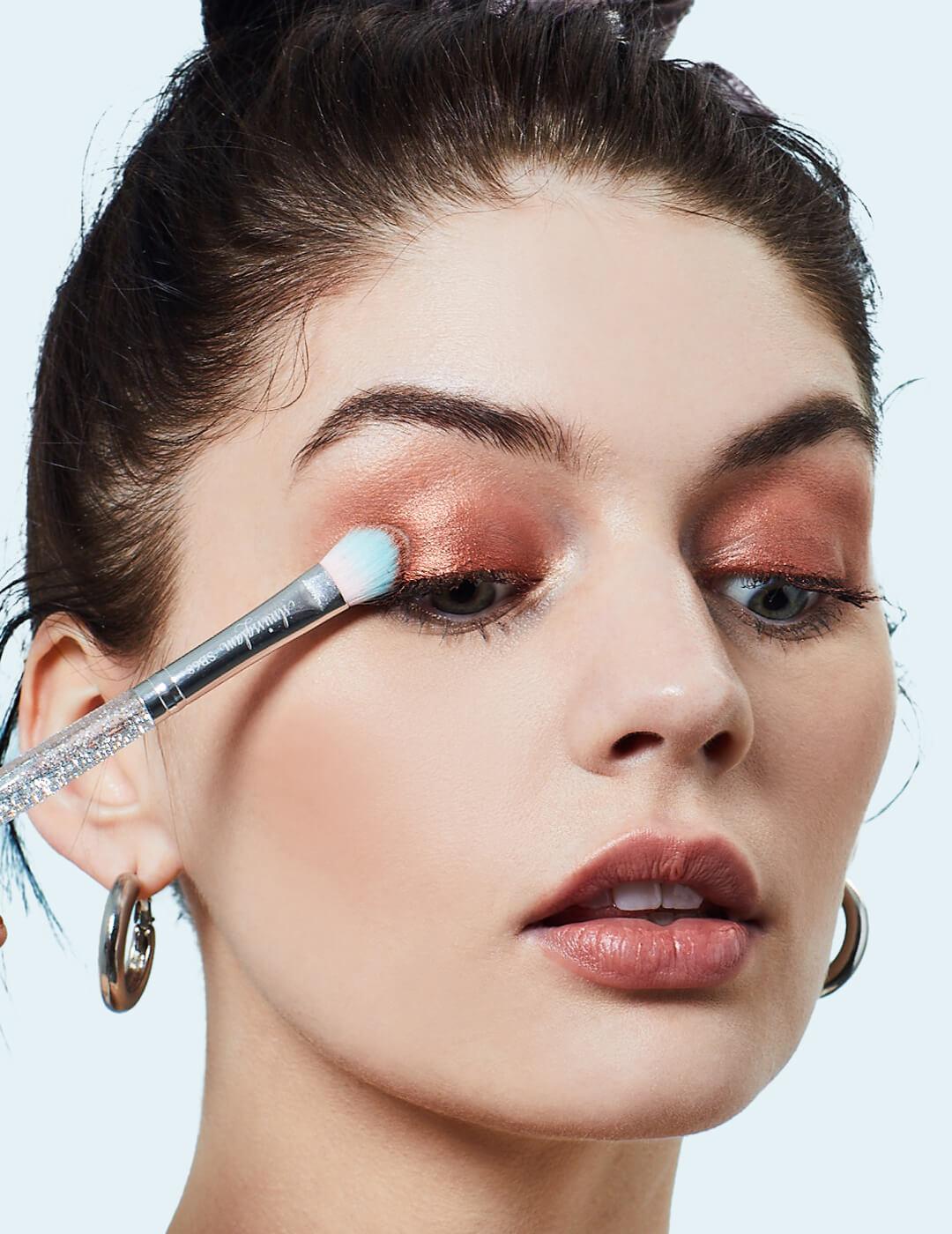 Close-up of a model applying shimmery nude eyeshadow on her eyelids using a small brush Desktop