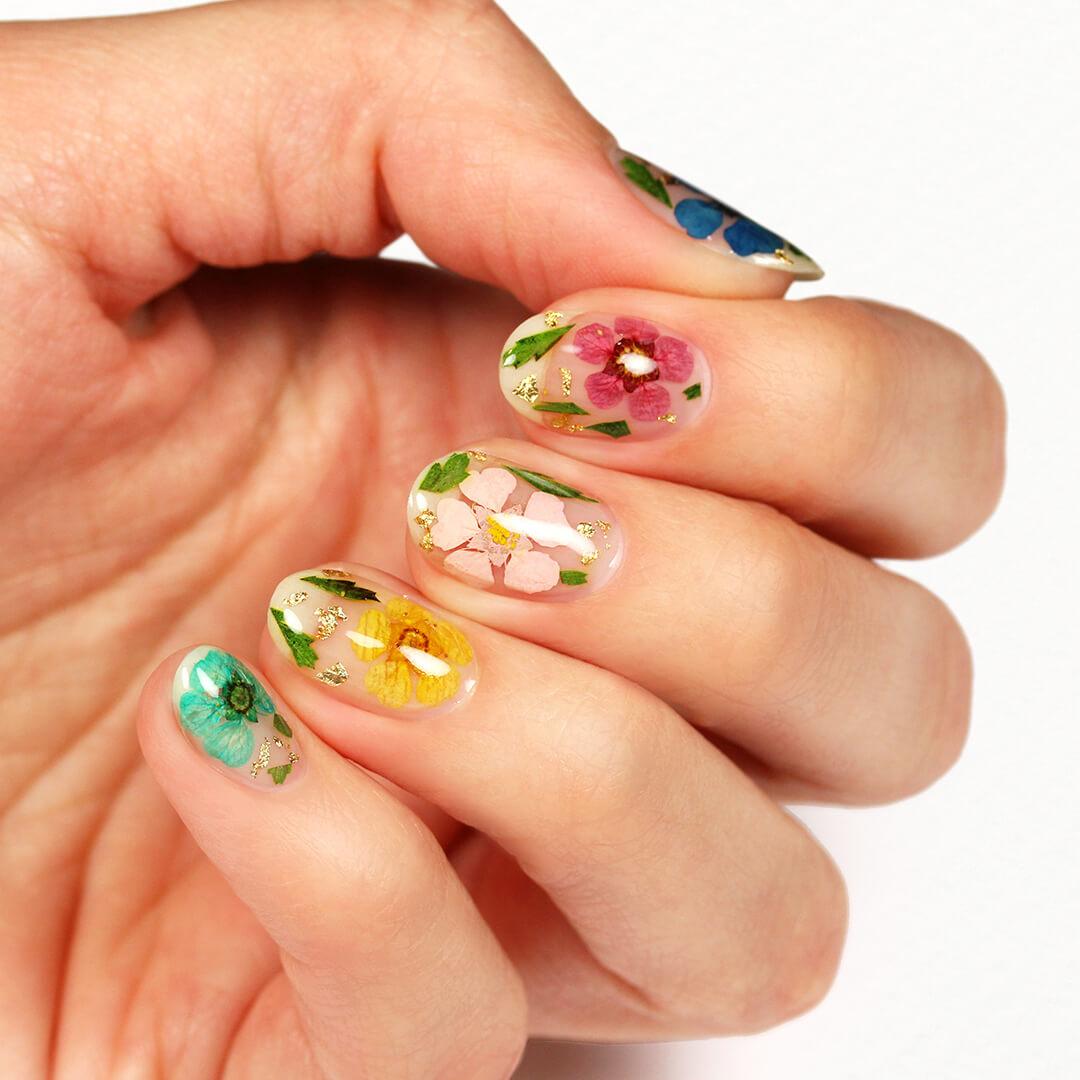 An image of a model's fingers with dried flowers and gold leaf nail art Mobile
