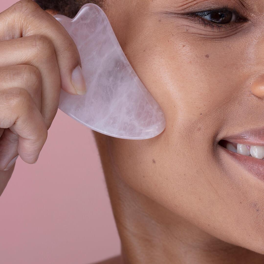 Close-up image of a woman using a pink quartz gua sha stone on her face Desktop