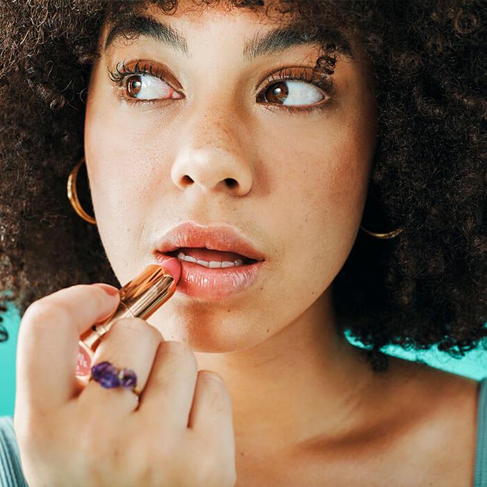 A close-up image of a curly-haired girl applying lipstick Mobile