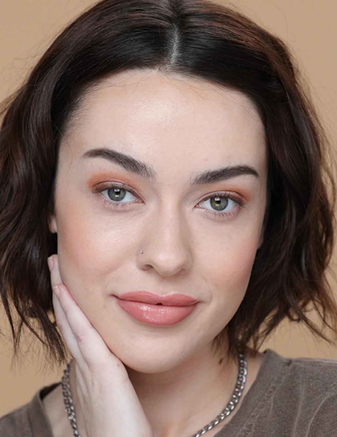 An image of a woman wearing natural makeup while touching her neck in one hand Mobile
