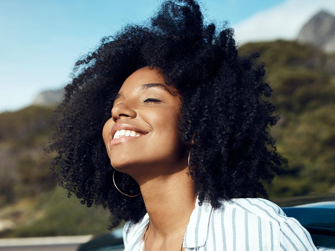 Close-up of a woman of color smiling in the sun against greenery background Desktop