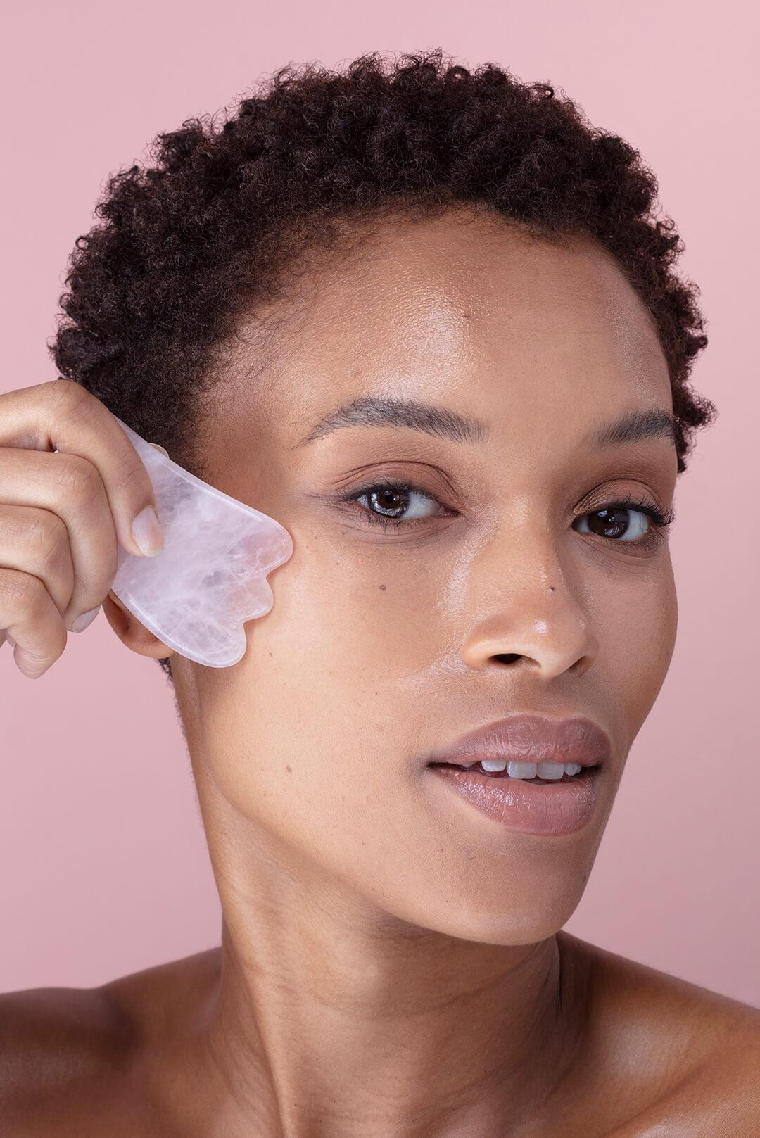 Close-up image of a woman using a pink quartz gua sha stone on her face Desktop