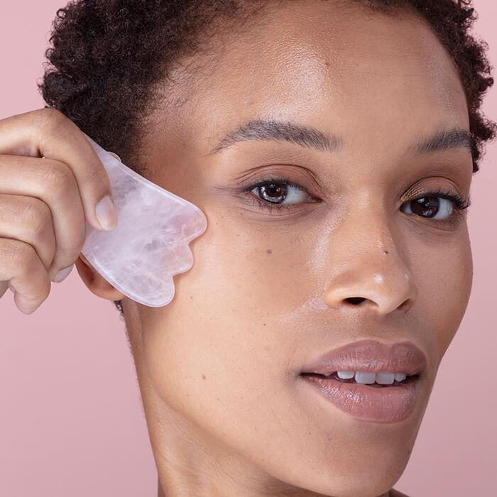 Close-up image of a woman using a pink quartz gua sha stone on her face Mobile