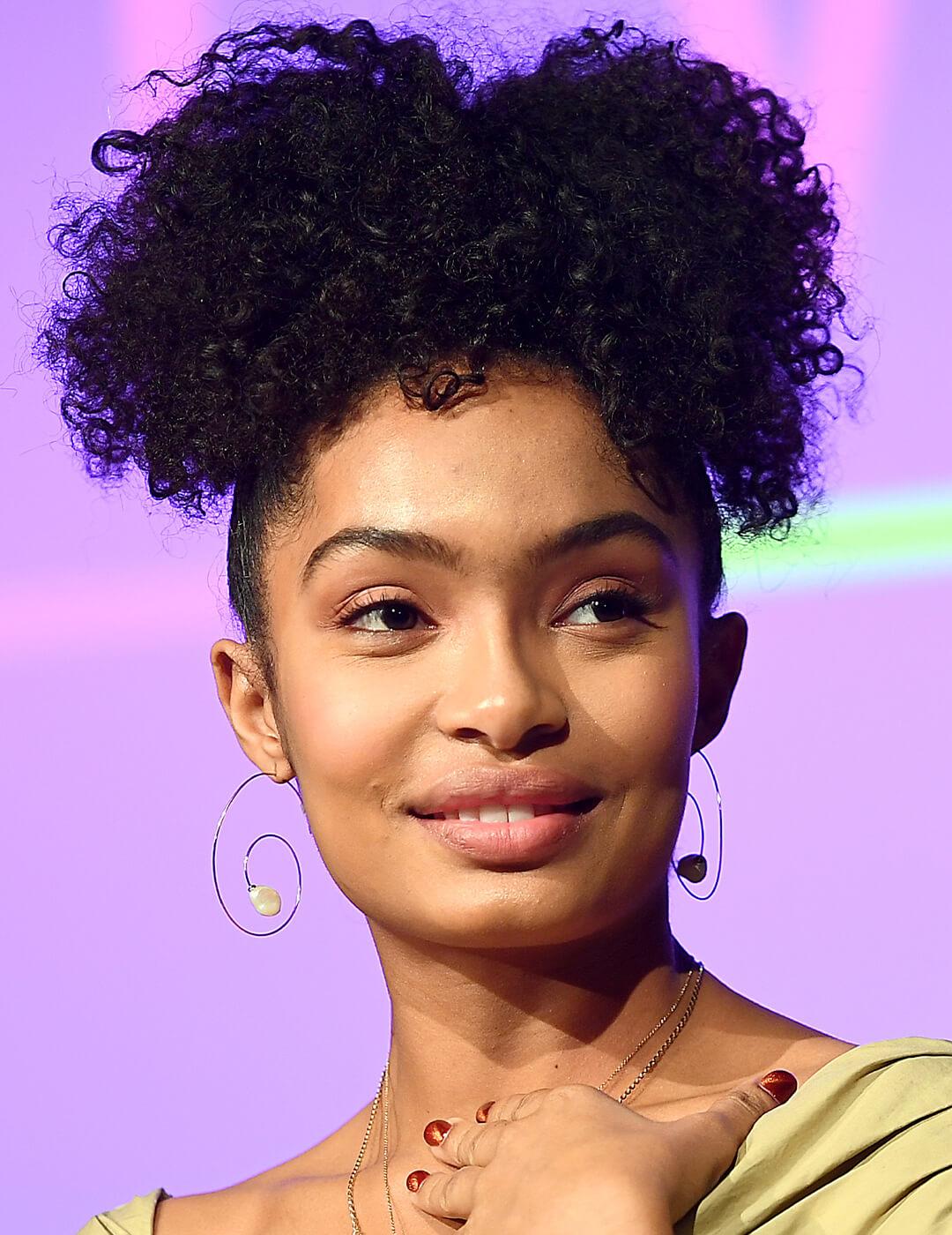 Yara Shahidi wearing a whimsical pair of earrings and pineapple, high ponytail hairstyle Mobile
