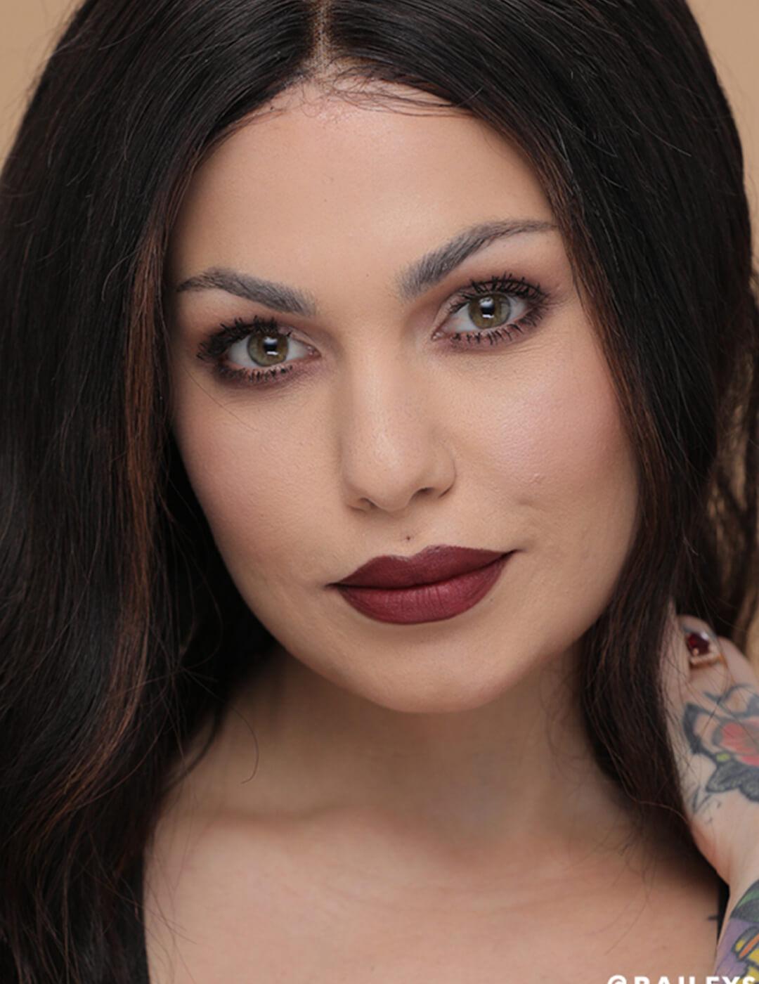 A photo of Bailey Sarian looking fierce while wearing red lipstick and touching her neck in one hand Desktop