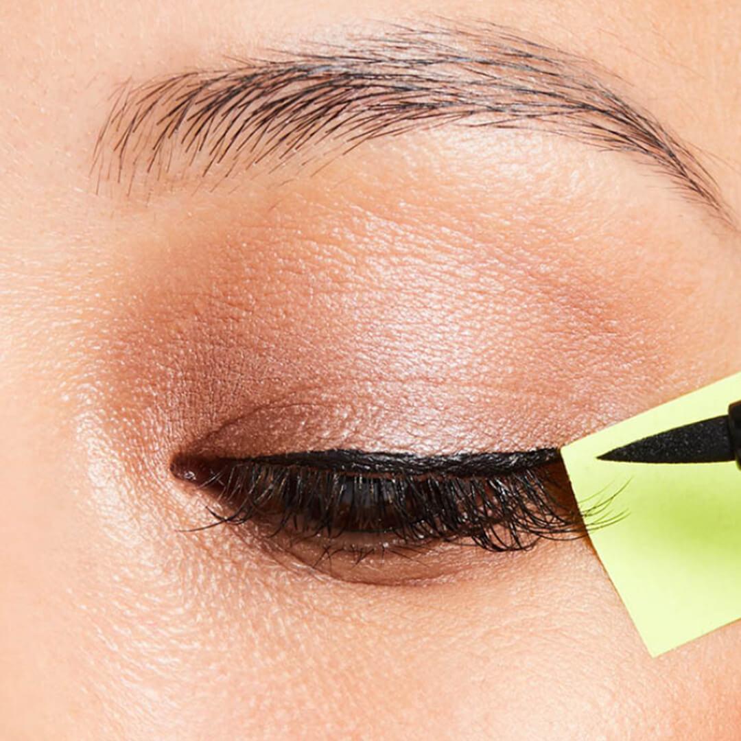 Close-up of woman's eyes, applying liquid eyeliner with sticky note as guide Desktop